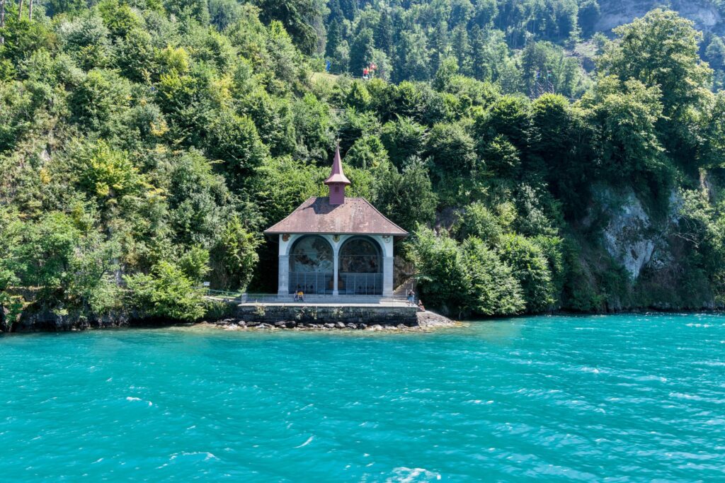 Serene chapel by turquoise Lake Lucerne, surrounded by lush forest, Switzerland.